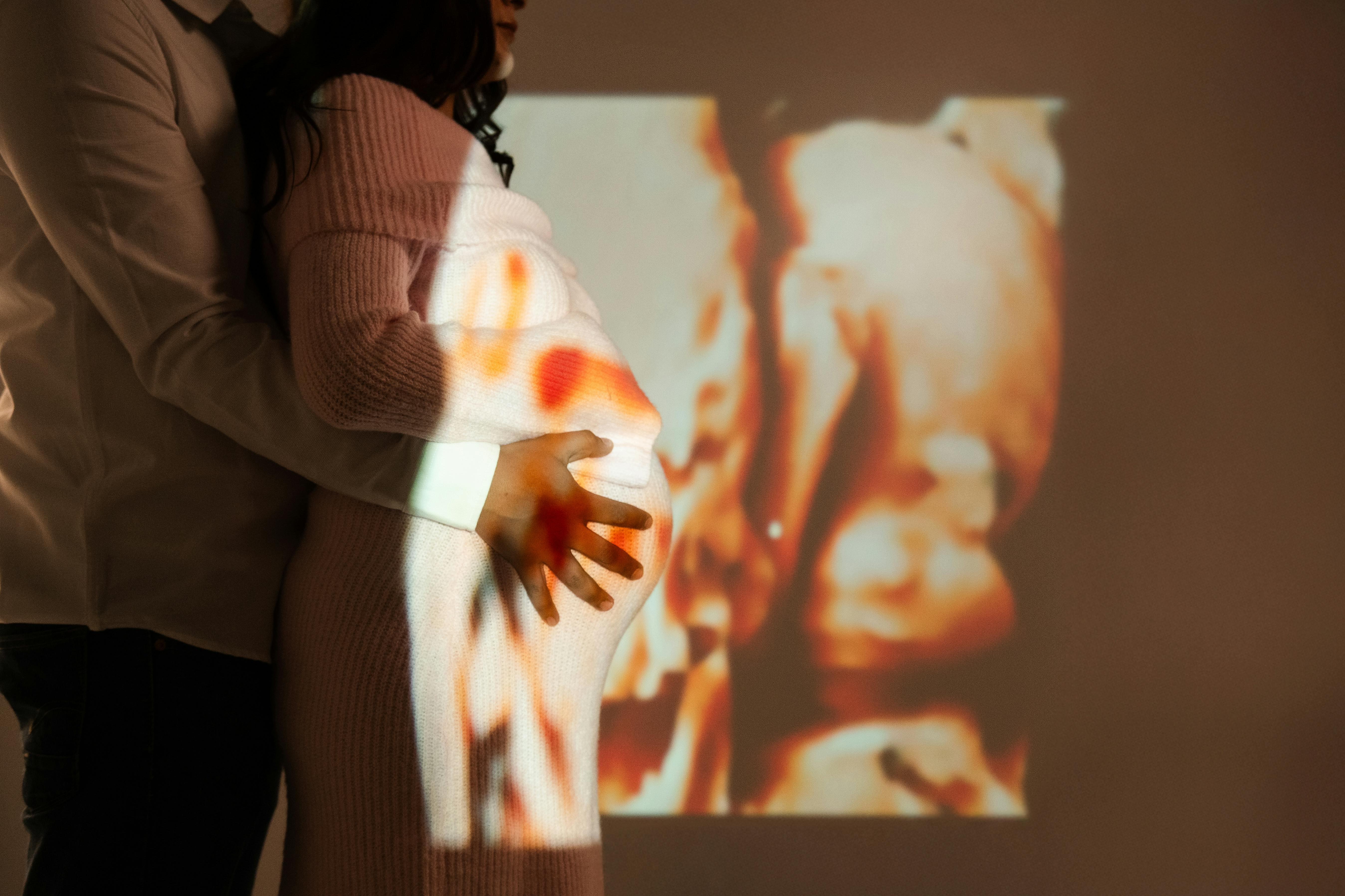 A couple embraces with a baby's ultrasound projected on a pregnant belly.