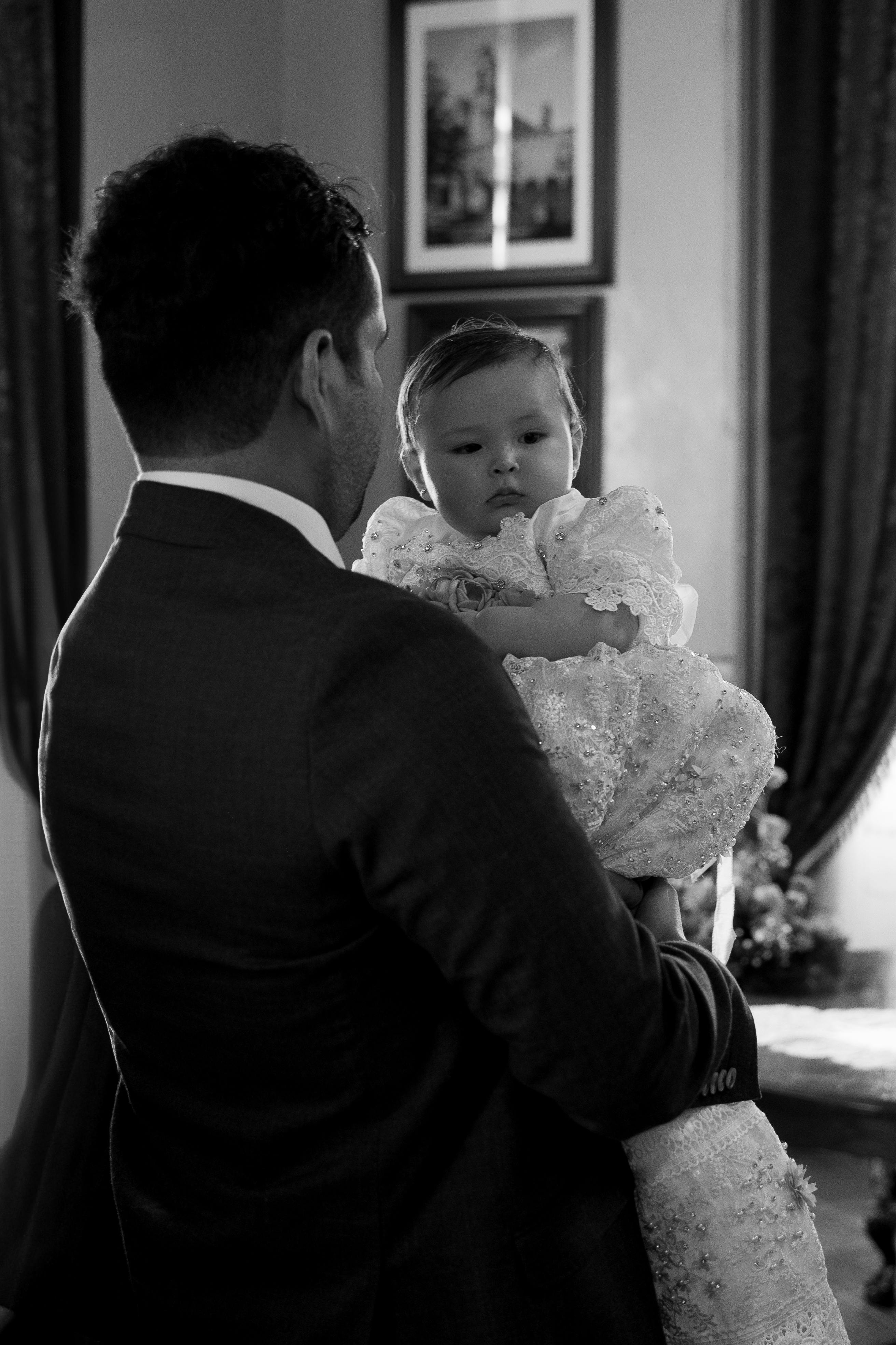 Black and white image of father holding baby in elegant setting.